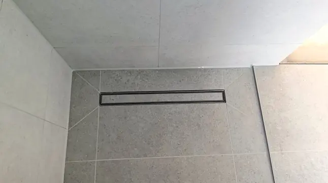 Bodengleiche Dusche mit Rinne, darin eine Fliese aus dem Bodenbelag