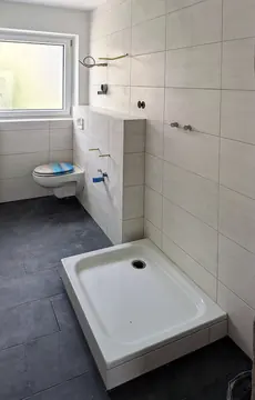 Duschwanne, geflieste Vorwand und WC im hellen Bad